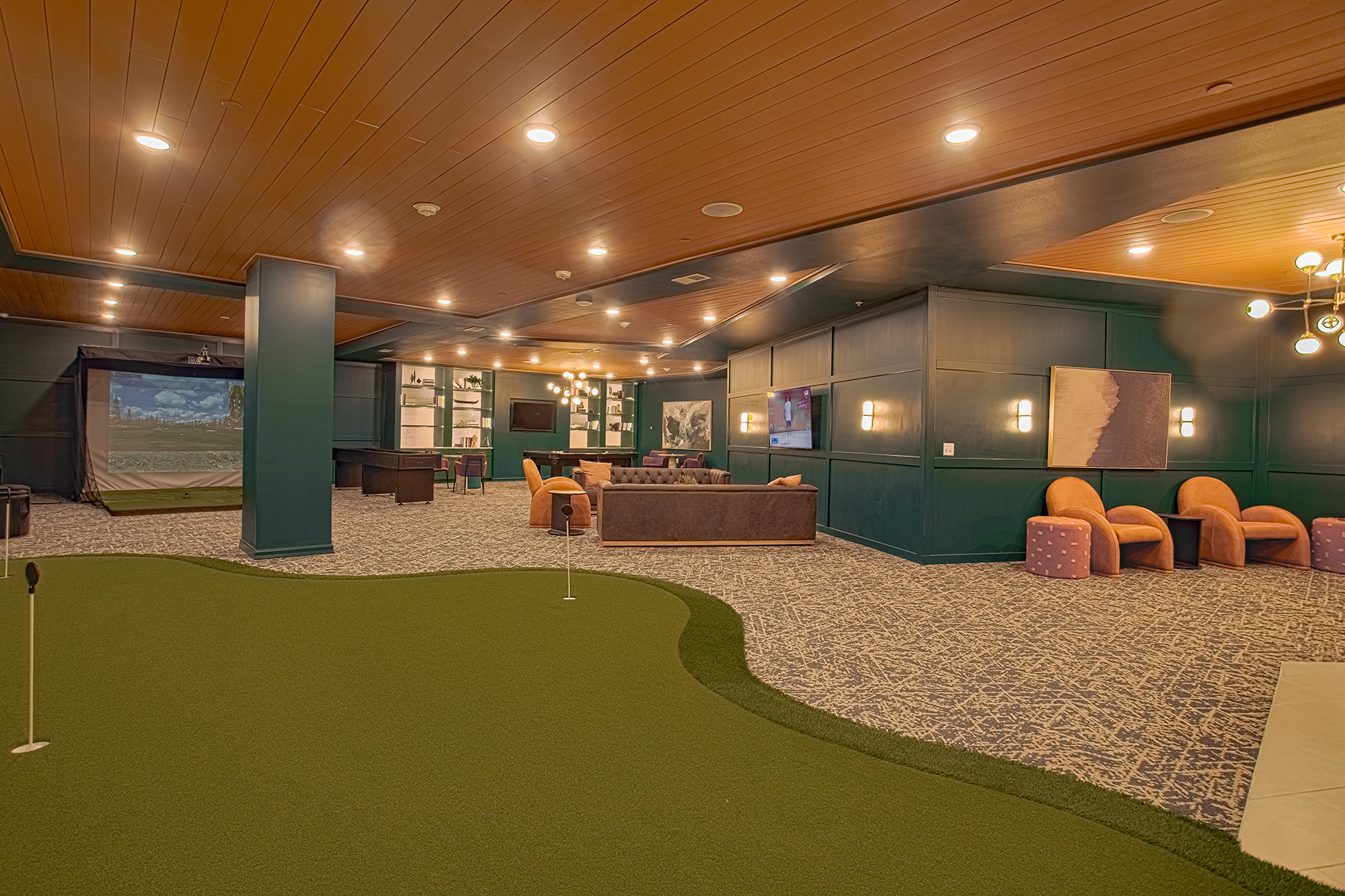 Alt text: Entertainment lounge at Vantage Anderson by HILLS Properties in Anderson, Ohio, featuring an indoor putting green, golf simulator, comfortable lounge seating, large TVs, and modern resident gathering spaces.