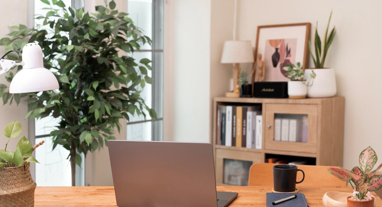 A stylish and bright home office workspace featuring a laptop on a wooden desk with abundant plants and minimalist decor.