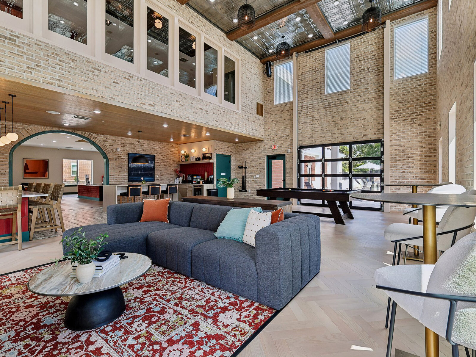 Spacious clubhouse lounge with sofas, tables, brick walls and a high ceiling.