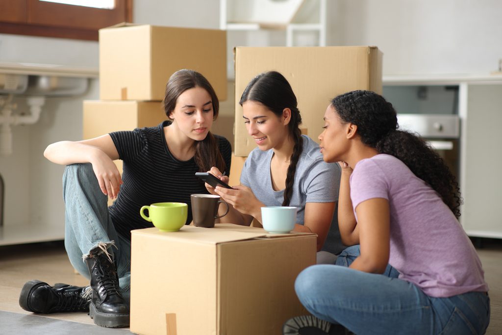 A group of friends search for an apartment together next to packed boxes.